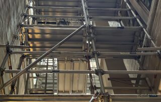Aluminium scaffolding installed in a narrow laneway between buildings, viewed from ground level.