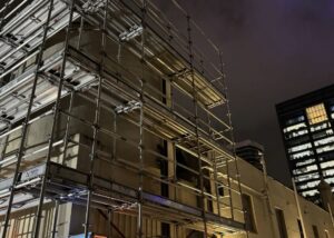 Night view of a fully erected scaffolding system around a commercial building with safety lighting.