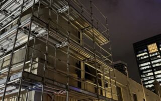 Night view of a fully erected scaffolding system around a commercial building with safety lighting.