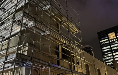 Night view of a fully erected scaffolding system around a commercial building with safety lighting.