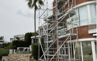 Beachfront residential building with full-height aluminium scaffolding installed for external access and maintenance.