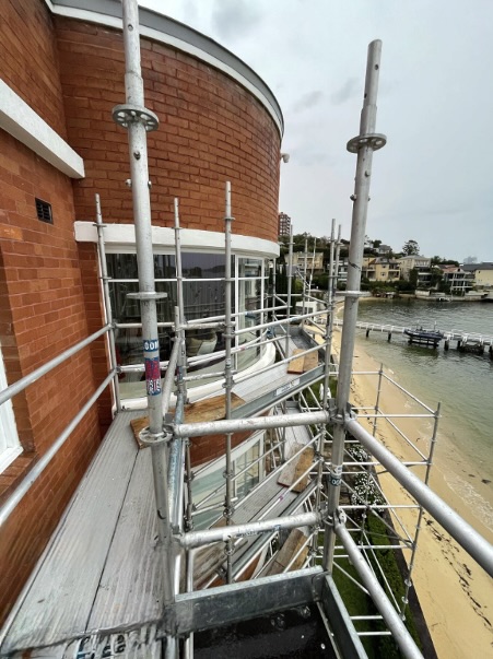 Curved Aluminium Balcony Scaffolding for Beachfront Home Scaffolding system installed along a curved residential balcony overlooking a beach and waterfront.