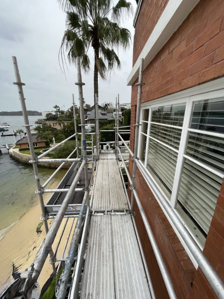 Beachside Residential Aluminium Scaffolding Walkway Aluminium Scaffolding platform installed along a red-brick residential wall facing a beachfront with palm trees and ocean views.