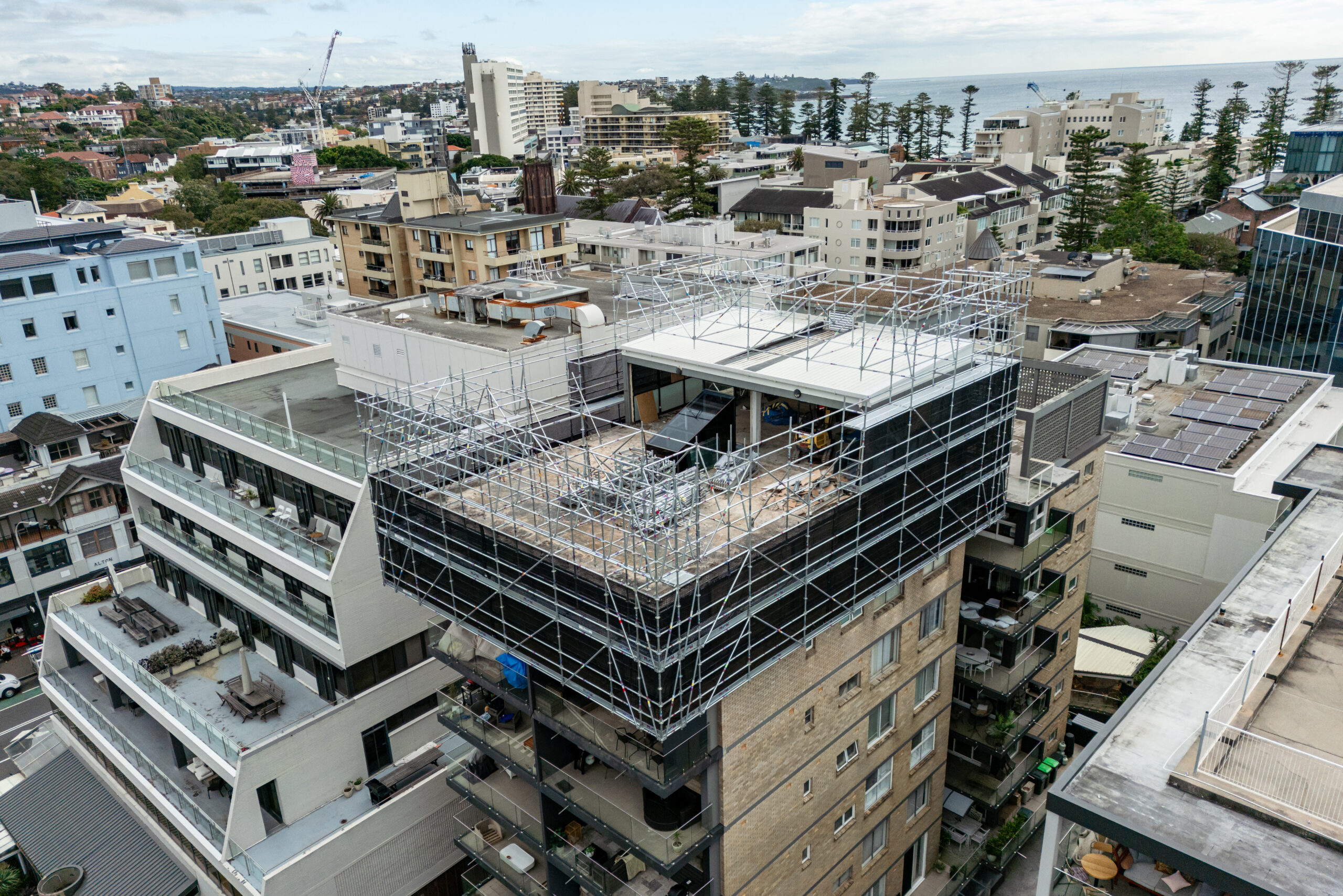 Aerial View Cantilevered Rooftop Scaffold – Manly Apartment Renovation, Sydney North Shore Aerial view of cantilevered rooftop scaffold on apartment building in Manly Sydney with harbour in background